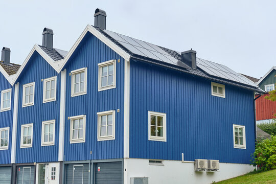 Karlskrona, Sweden - 14 September 2025: View of traditional blue wooden houses with solar panels on the roof, white window frames and heat pumps under an overcast sky.