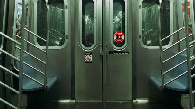 Center doors of empty subway car flanked by blue seats and stainless handrails, stop sticker on door, sterile green lighting,