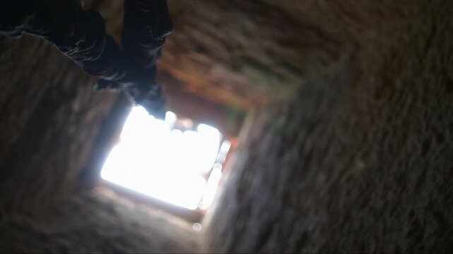 Low angle view from the bottom of a dark, stone well showing a rope and the bright sky above