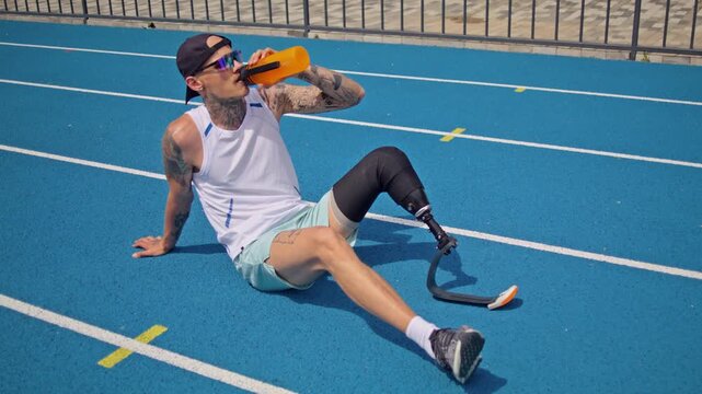 Man jogger with bionic leg prosthesis drinks water on track