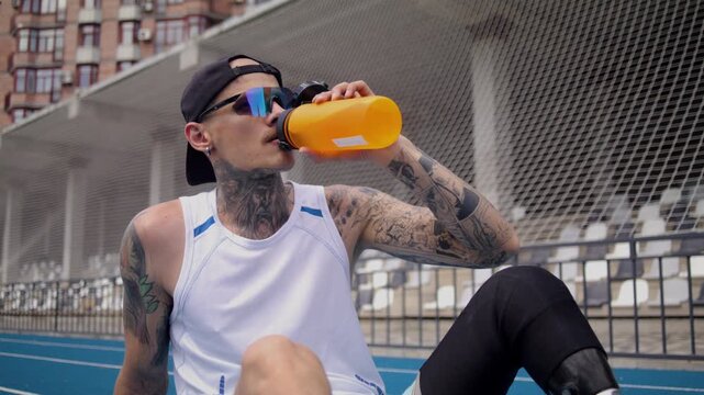 Sportsman with bionic leg prosthesis sips water sitting on track
