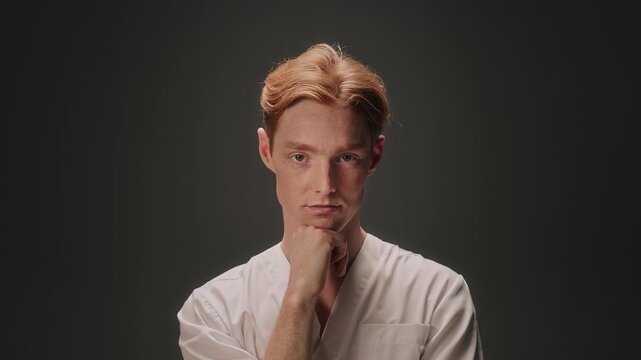 Calm studio portrait of white male thinker with chin resting on hand, neutral backdrop, steady gaze, quiet reflective mood, subtle