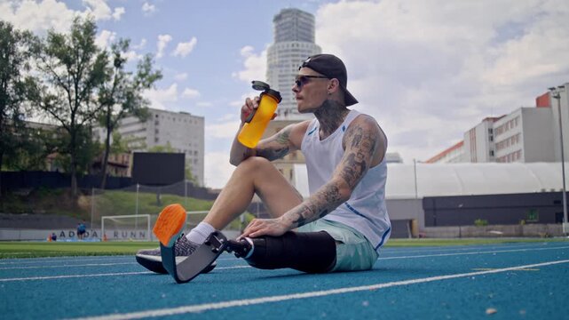 Man athlete with bionic leg prosthesis drinks water on track