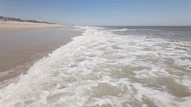 Waves crash in slow motion onto sandy shore under clear blue sky