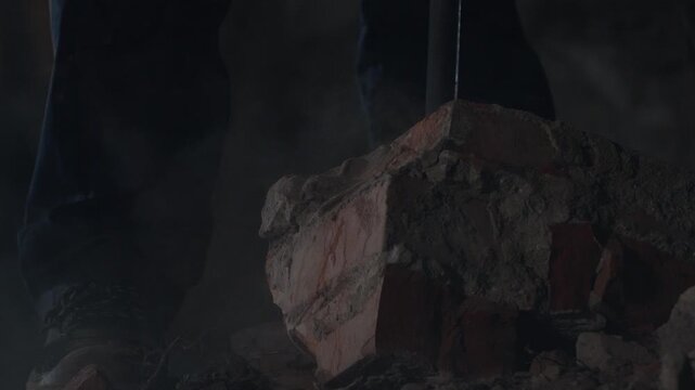 Closeup sledgehammer striking brick with rubble and dust flying heavy impact shot showing boots and legs of worker