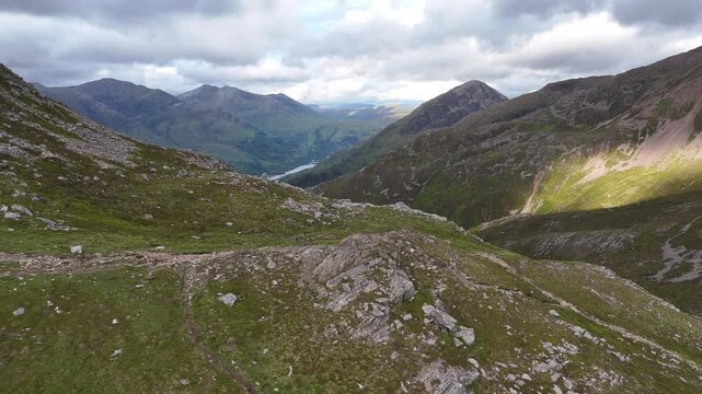 This aerial drone footage captures a spring afternoon in the Scottish Highlands. The camera performs a dolly lateral left and boom up, revealing a rugged, rocky landscape near the Pap of Glencoe.