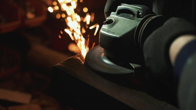 Closeup angle grinder sparks on steel held by gloved hand heavy metalwork in workshop with bright orange shower