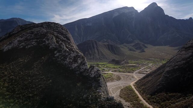 Aerial drone slowly reveals the rugged Huasteca Canyon landscape in Monterrey, with the dry Santa Catarina River basin cutting between dramatic arid mountain ranges and distant forests under a vivid b