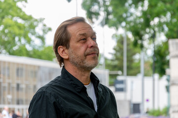 Naklejka premium Man about 55 years old looking into the distance with urban and tree background.