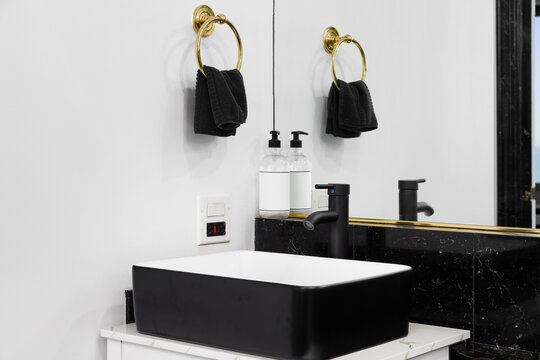 A bathroom detail with a black faucet over a white and black vessel sink, a white cabinet, and a black granite backsplash.