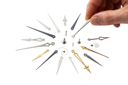 A hand holds a small metal object among various clock parts on a table indoors.