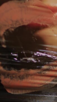 Close-up of woman's teeth biting on a screen of plastic wrap and leaving behind a pink lipstick marks