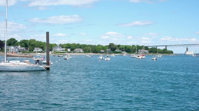 Sailboats and yachts anchored in scenic harbor with suspension bridge