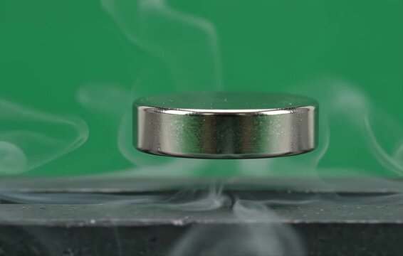 A metallic disc levitating above a surface with swirling smoke against a green background.