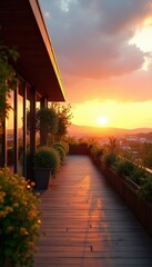 Obraz premium Modern terrace balcony with wooden floor at sunset. Orange sky and sun over cityscape. Green plants and trees line the walkway. Glass building reflects warm light.