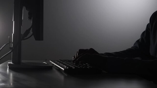 Person working late night on computer keyboard, with backlight illuminating hands and monitor, representing cybersecurity, programming, data breach, or digital crime