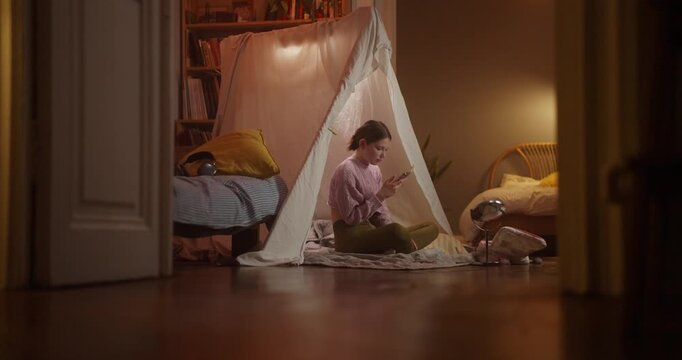 Child using a smartphone inside a cozy indoor tent