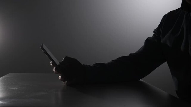 Anonymous person silently holding and interacting with a glowing smartphone screen in a dark, dimly lit environment, symbolizing data security, cybercrime, and digital privacy concerns