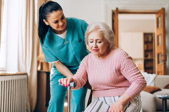 Beautiful caregiver helping elder woman standing with walking cane