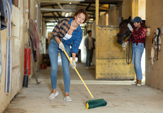 Woman working a horse stable - cleaning floor with brush