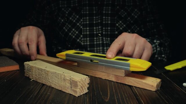 Person using a yellow level tool to measure wood pieces on a dark wooden table, showcasing precise alignment and craftsmanship in a workshop setting
