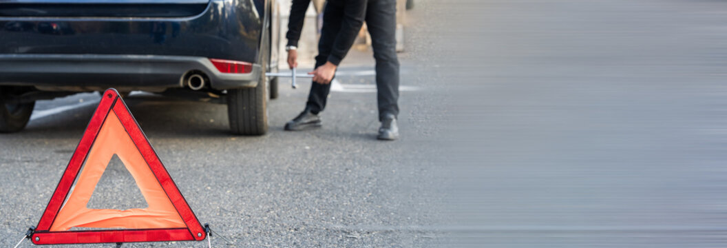 A road sign next to a broken-down car, indicating caution and alerting drivers to a vehicle malfunction or potential hazard on the roadway.
