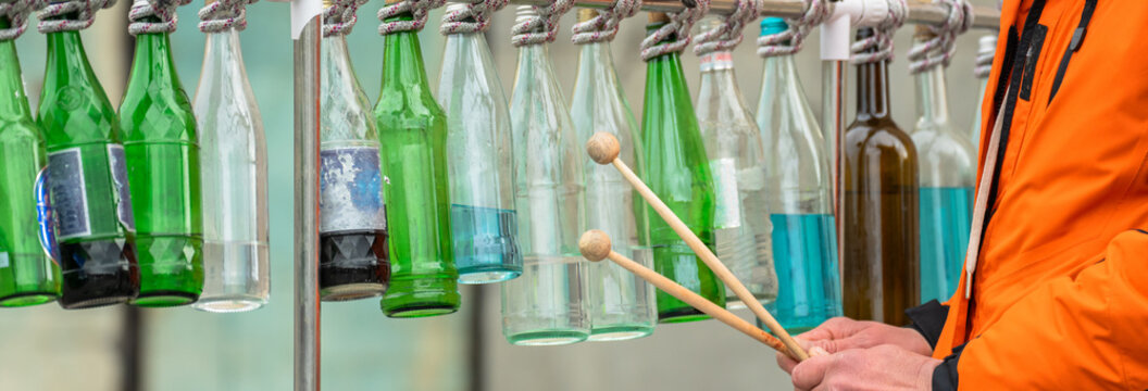 Street musician performing with glass bottles as instruments, showcasing creativity, urban street culture, improvisation, and live public entertainment in a city environment.