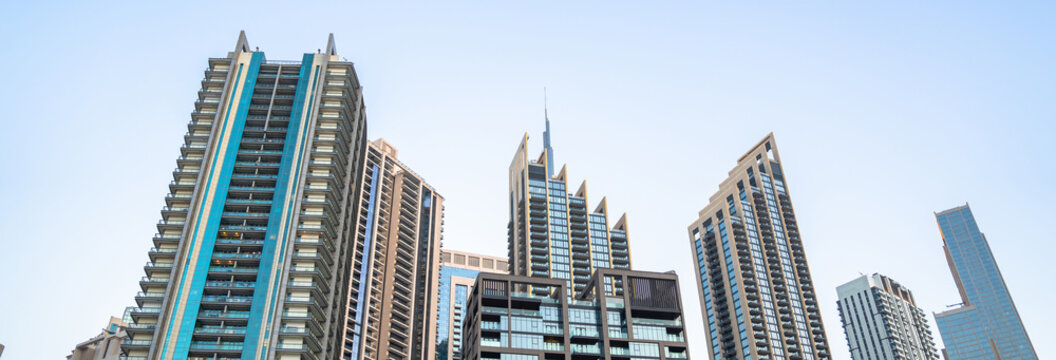 Modern skyscrapers rising in dense urban city skyline, tall glass buildings reflecting sunlight, metropolitan architecture, financial district, and contemporary city development concept.