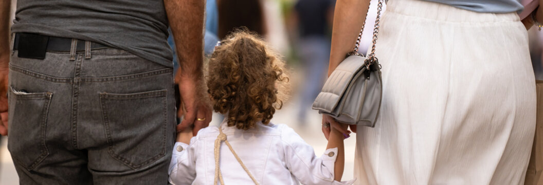 Family walking together outdoors, parents holding child&rsquo;s hands while strolling in a park, warm family bonding, happiness, and everyday lifestyle concept.