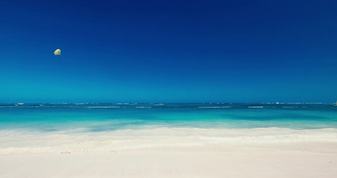 Caribbean vacation tropical beach and turquoise ocean under clear blue sky with parasailing parachute in the sky