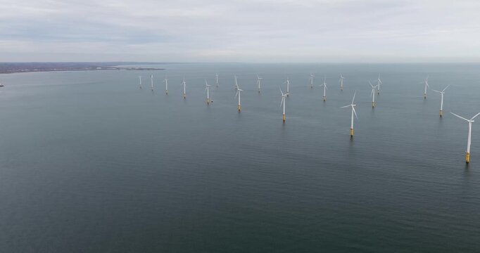 Aerial panning footage of offshore wind farm near Redcar Middlesbrough UK showing multiple turbines in the sea with distant coastline visible across calm water in a wide landscape scene