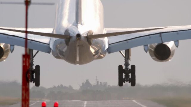 Passenger jet airplane landing on asphalt runway with smoke from tires under bright daylight, telephoto lens shot from behind, slow motion