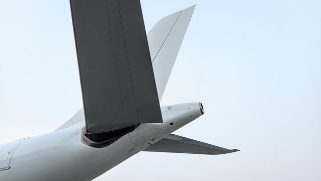 Detailed low-angle view of an aircraft tail section featuring the rudder, vertical stabilizer, horizontal stabilizer, and APU exhaust, highlighting the aerodynamic design and engineering precision