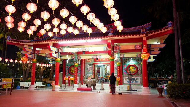 Night view of a Chinese shrine illuminated by rows of red hanging lanterns with a person standing in front.
