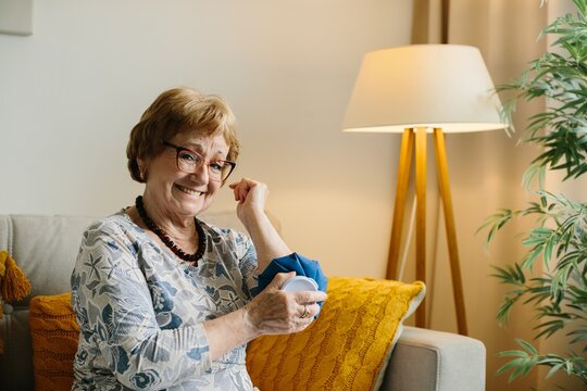 Senior woman smiling applying ice pack on arm