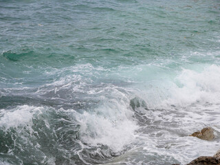 Naklejka premium Powerful ocean waves swirl around coastal rocks creating white sea foam and textured turquoise water. Natural seascape background suitable for travel, marine, environment, and nature-related themes.