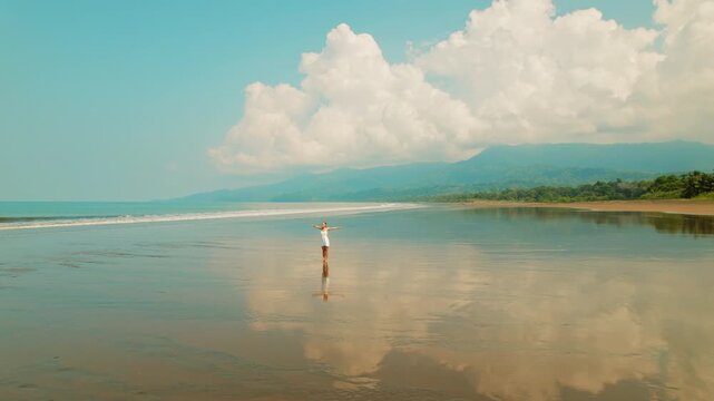 Happy woman enjoying life while standing with arms open on reflective beach in Costa Rica