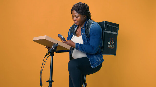 African American courier delivers package using bicycle and modern pos machine ensuring contact-free service, delivery woman providing nfc terminal for convenient wireless payment for food delivery