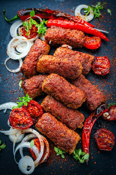 Traditional original artisan grilled cevapi made of spicy minced meat onion, roasted tomato and chili served as close-up on a design plate
