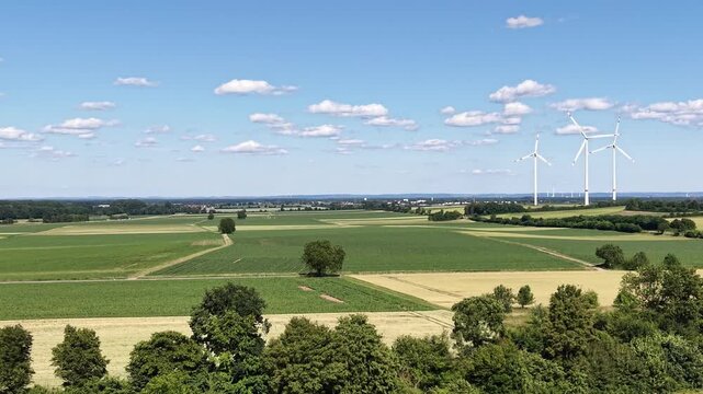 Drone video showcasing a vast agricultural landscape with cultivated crop fields, rural roads and modern wind turbines on the horizon. Scenic countryside panorama highlighting sustainable energy and m