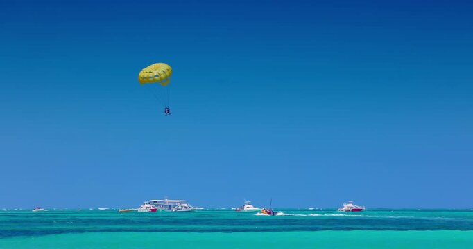 Parasailing with a yellow parachute high in the blue sky over the turquoise Caribbean sea, summer water sport activity in Punta Cana tropical beach shore