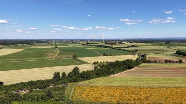 Drone video showcasing a vast agricultural landscape with cultivated crop fields, rural roads and modern wind turbines on the horizon. Scenic countryside panorama highlighting sustainable energy and m