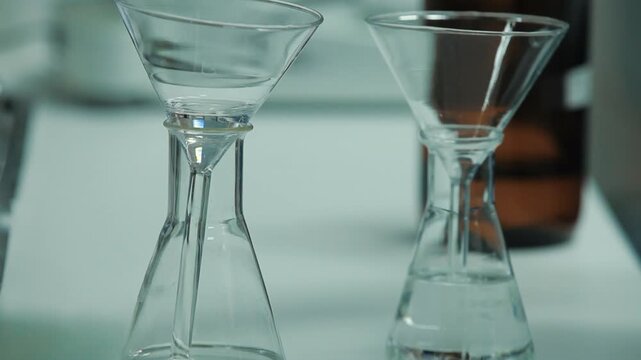 Close-up of pouring clear liquid into an Erlenmeyer flask through a glass funnel in a laboratory.