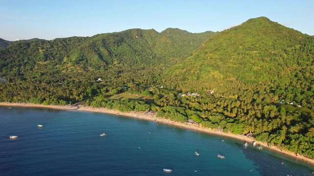 Aerial drone footage of Nipah beach, in Pemenang area, Lombok island, Indonesia, with flat quiet blue water, forests and mountains behind, at golden sunset