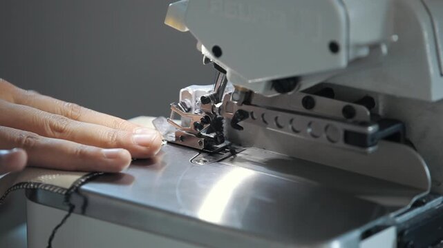 Macro shot of a seamstress sewing fabric edges with black thread using a professional serger machine.