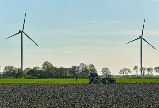 Middenmeer, Netherlands - 14 April 2026: View of Vattenfall wind turbines in the Wieringermeer polder with a tractor working in a ploughed field under a clear sky.