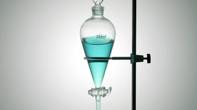 Close-up of a separatory funnel slowly swirled containing transparent cyan fluid, causing it to wave along the inner walls on grey ramp background