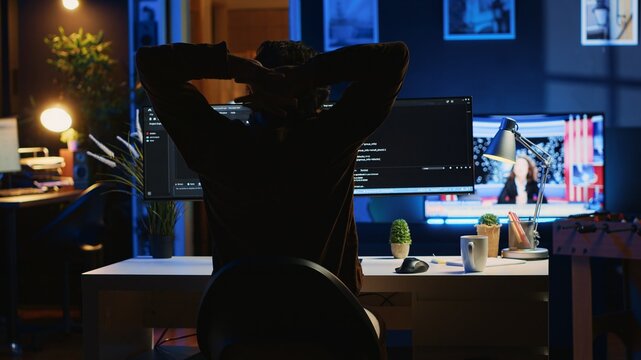 Man doing IT support job from home office, stretching after sitting on desk chair all day. Programmer loosening up, relaxing after typing on computer for long period of time, camera A