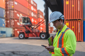 Fototapeta premium Forklift moves cargo between stacked shipping containers at a busy logistics shipping container terminal yard.