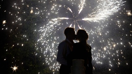 Naklejka premium Silhouette of bride and groom kissing with fireworks and wedding cake